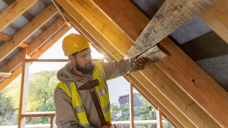 Artisan en plein travail sur une charpente en bois, renforçant la structure des combles pour une future transformation en espace habitable.